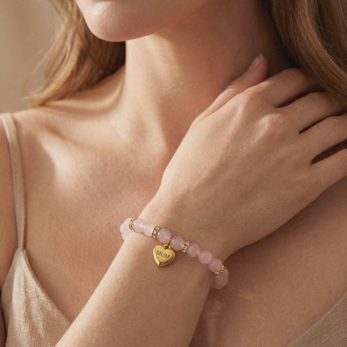 Rose quartz beaded bracelet with gold spacer beads and a MUM heart charm worn on a wrist.