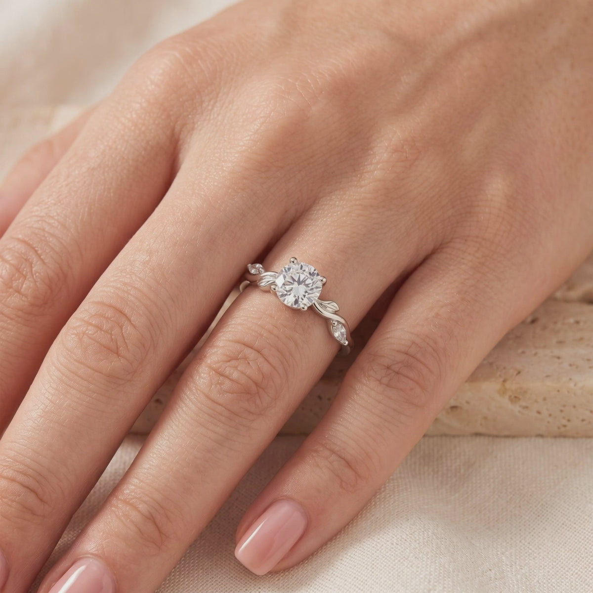 Silver leaf-motif ring with a round clear center stone worn on a hand over neutral fabric.