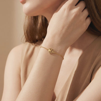 Gold-tone chain bracelet with a heart-shaped script charm, shown worn on a woman's wrist.