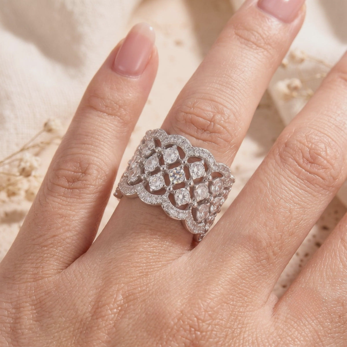 Wide silver lattice ring with clear round stones and scalloped borders, worn on a finger.