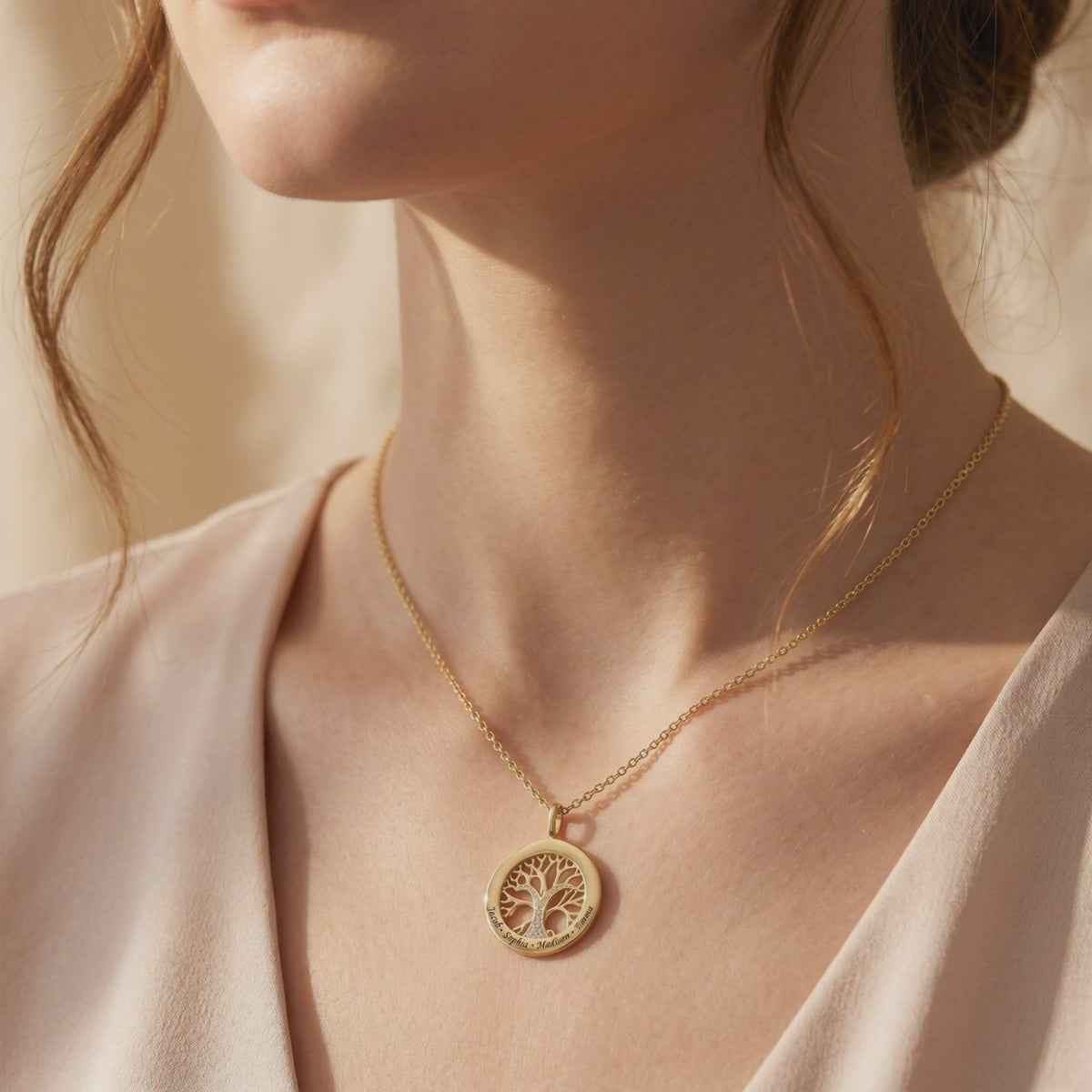 Gold-tone circular tree-of-life necklace worn at the collarbone, with engraved names around the pendant rim.