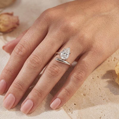 Pear-cut simulated diamond bypass ring in silver worn on a hand, with a round accent at the open end.