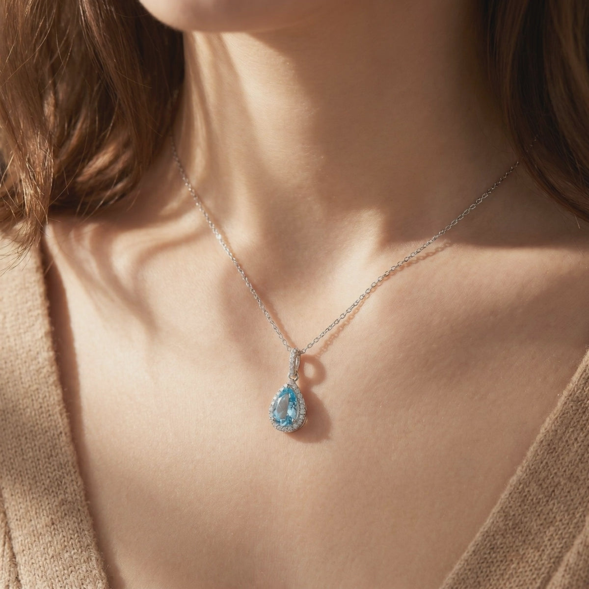 Model wearing a silver necklace with a pear-shaped light blue aquamarine pendant surrounded by a sparkling halo.