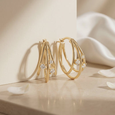 Pair of gold multi-row hoop earrings with round moissanite accents displayed upright on a beige surface.