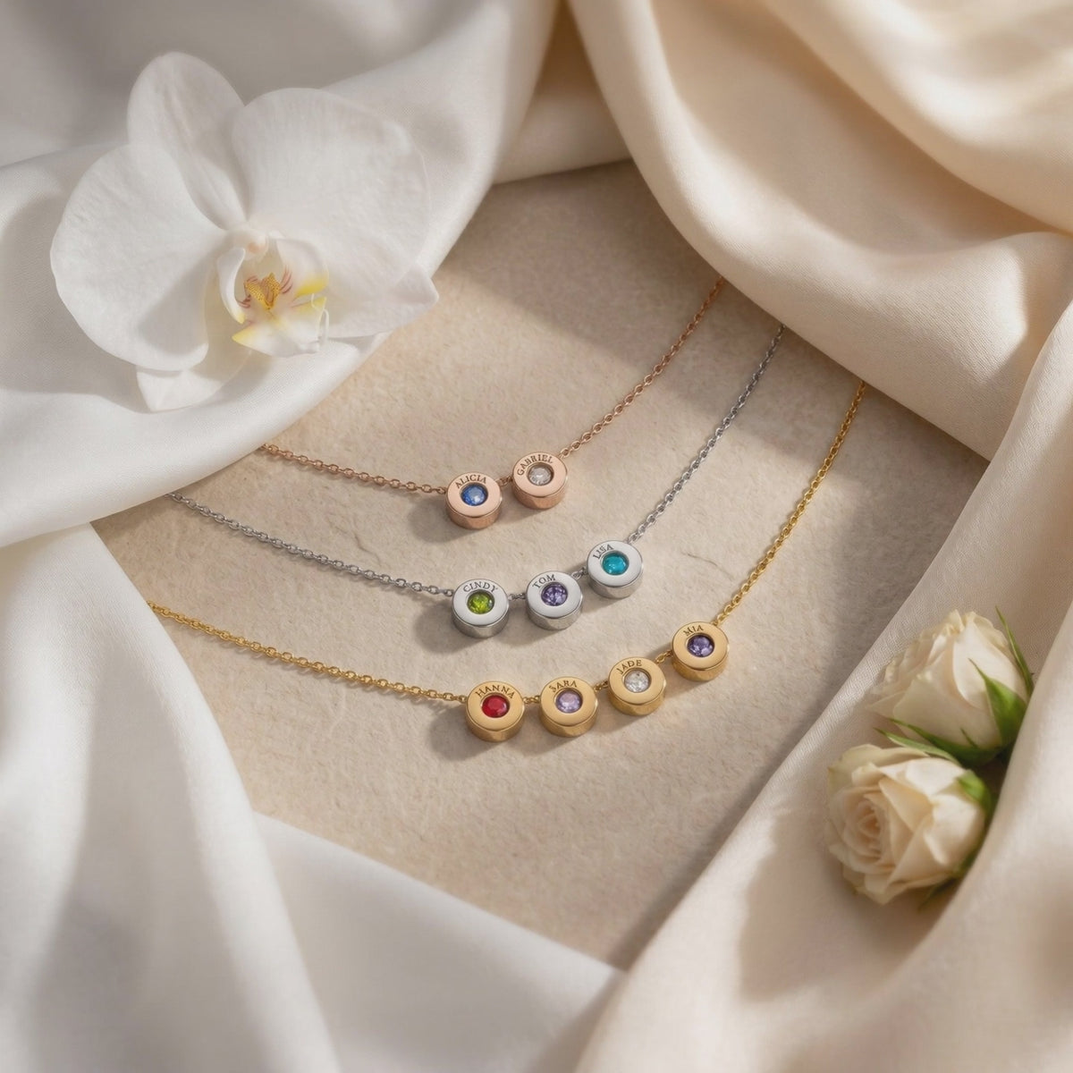 Three Lucenna necklaces in rose gold, silver, and gold finishes with engraved charms arranged on draped white fabric.