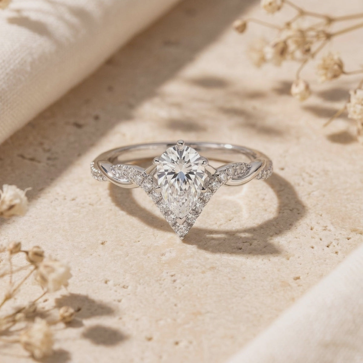 Silver pear-cut moissanite ring with a chevron pavé accent and twisted band, resting upright on a beige stone surface.