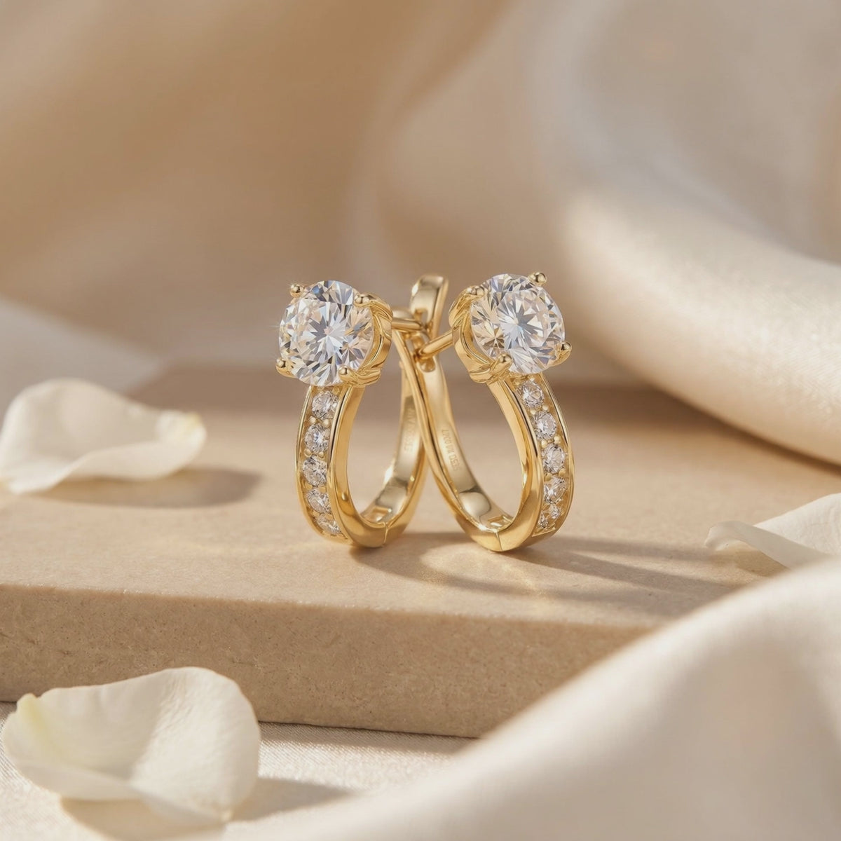 Pair of gold-toned hoop earrings with round moissanite centers and accent stones on a beige pedestal.