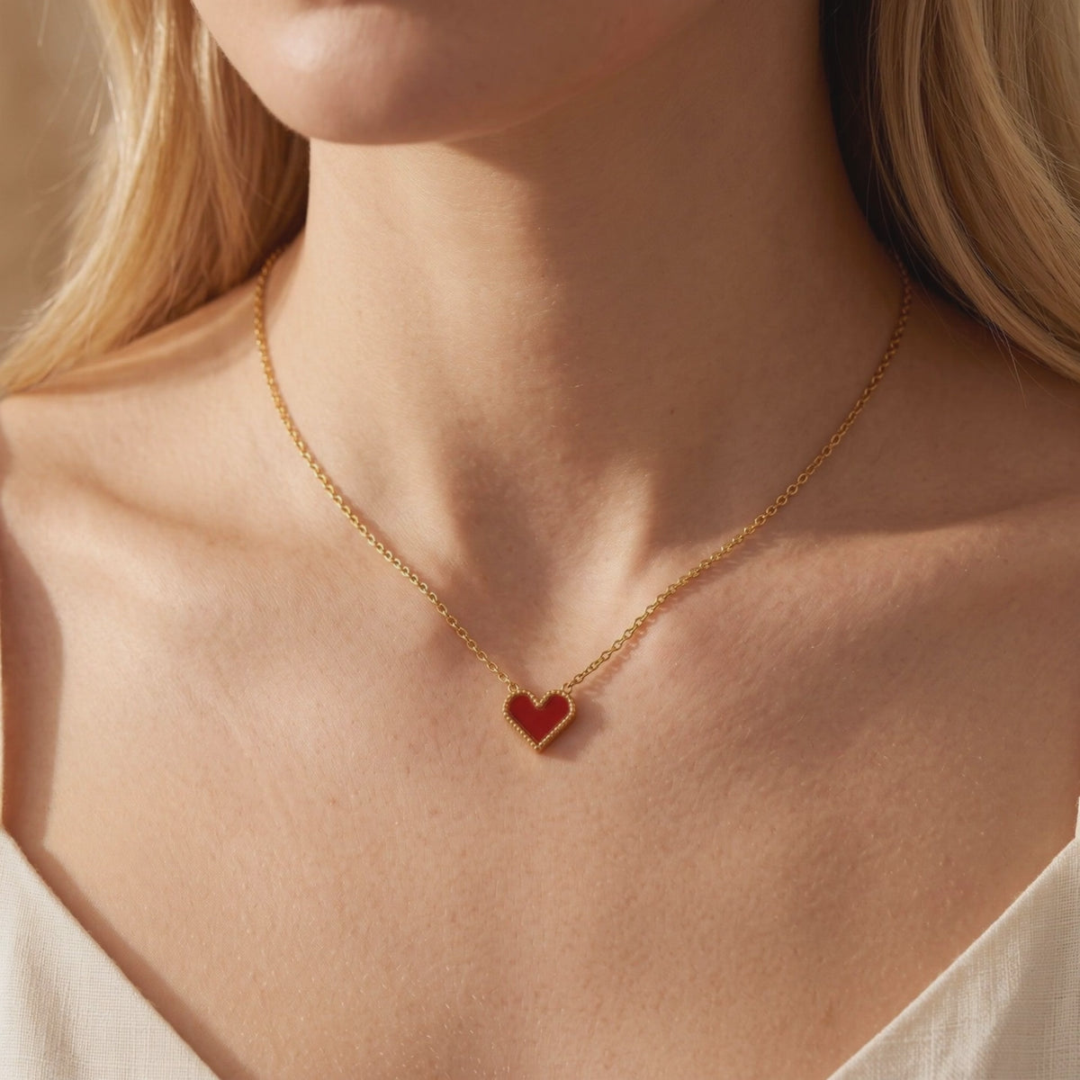 Model wearing a gold chain necklace with a red heart pendant framed by a beaded gold border.