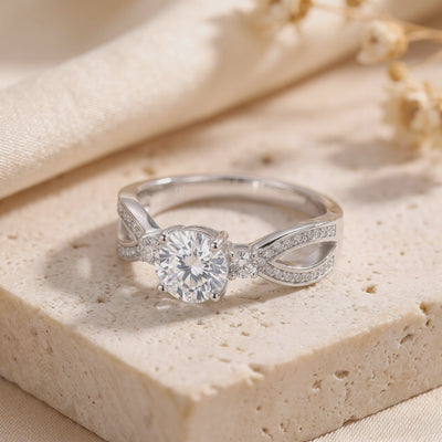 Silver ring resting on a textured stone, featuring a round clear center stone and micro-pavé split bypass band.