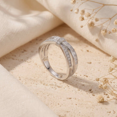Video preview of the silver criss-cross ribbon ring standing upright on a beige textured stone surface.